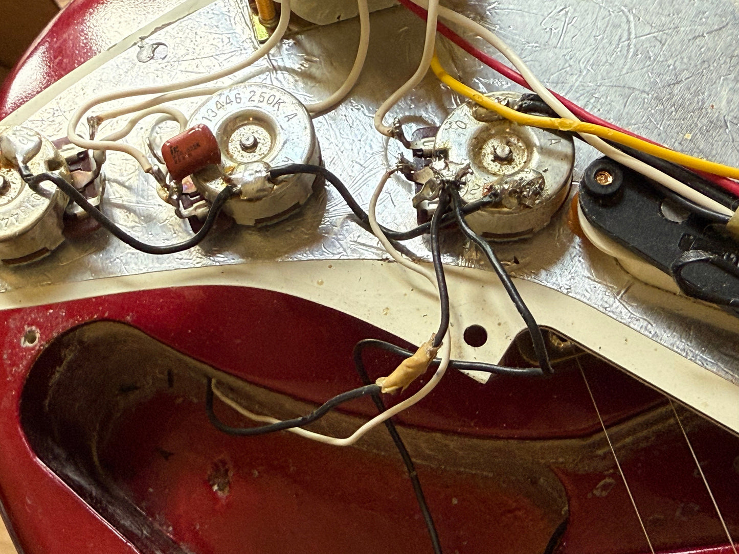 Close-up of guitar wiring and components on a red guitar body.