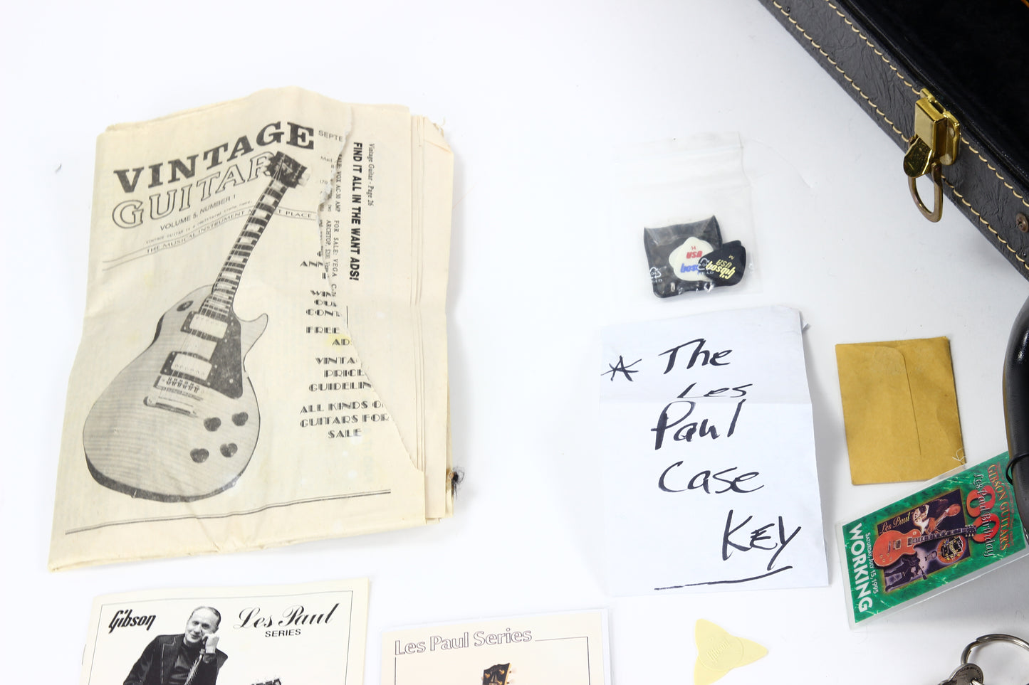 Collection of vintage guitar memorabilia including a case key, posters, and a book on a white surface.