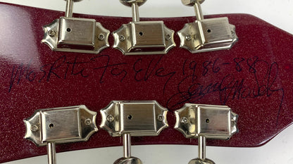 Close-up of a guitar headstock with six silver tuning pegs on a dark red glitter finish, featuring a handwritten inscription in black marker by Semie Mosely