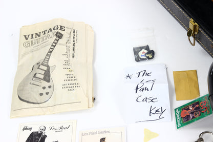 Collection of vintage guitar memorabilia including a case key, posters, and a book on a white surface.