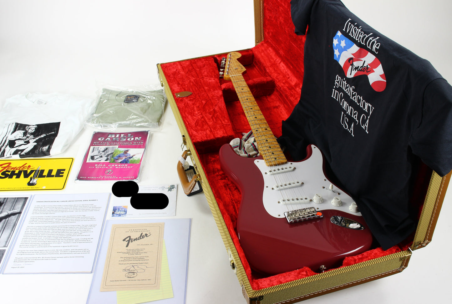 Fender guitar in a case with a t-shirt and promotional materials on a white background