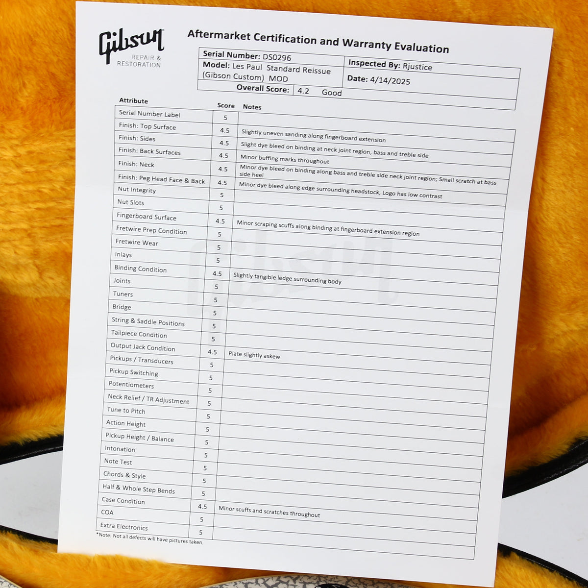 Gibson aftermarket certification and warranty evaluation form displayed next to a packaged headstock and receipt, set against the gold interior of a guitar case with part of a silver-and-black electric guitar visible.
